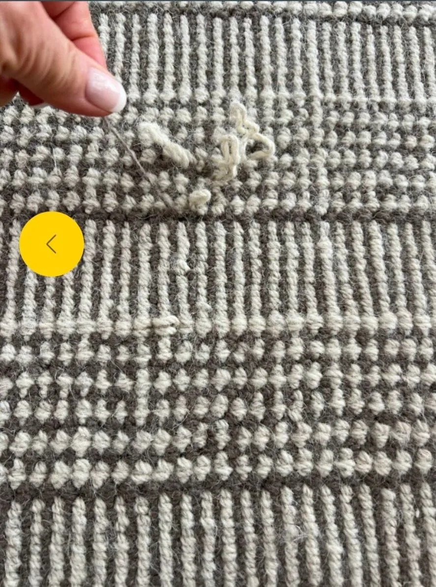 Hand lifting loose loops on a grey and cream flatweave rug