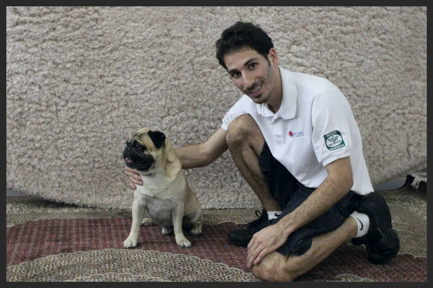 Our technician kneeling on an Oriental rug with a customer's pug at the shop